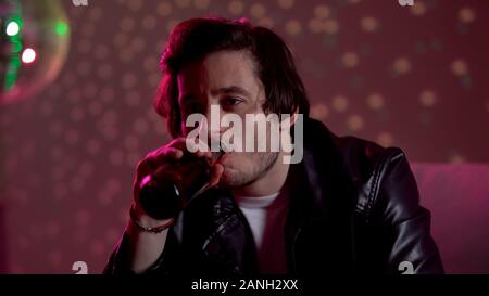 Sconvolto pensieroso uomo bere birra al night club discoteca party, pensare al problema Foto Stock