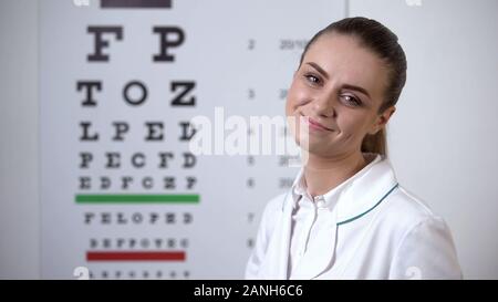 Oculista sorridente in posa vicino al grafico oculare in visione professionale clinica Foto Stock