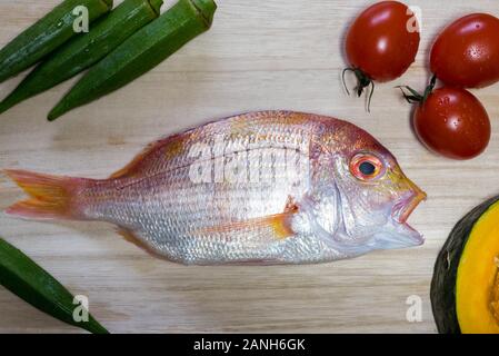 Un pesce intero pronto per essere cucinato con verdure intorno. Foto Stock