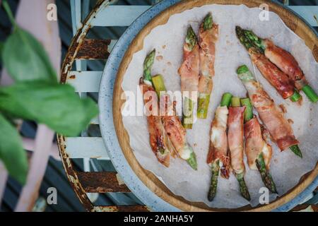 Cibo a buffet - prosciutto di Parma e mozzerella avvolto asparagi serviti su un piatto su una panchina da picnic rosa. Disposizione piatta Foto Stock