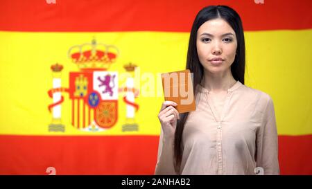 Grave donna asiatica mostrando passaporto contro Spanish flag di sfondo, la migrazione Foto Stock
