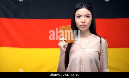 Grave femmina asiatica mostrando passaporto contro bandiera tedesca sfondo, close-up Foto Stock