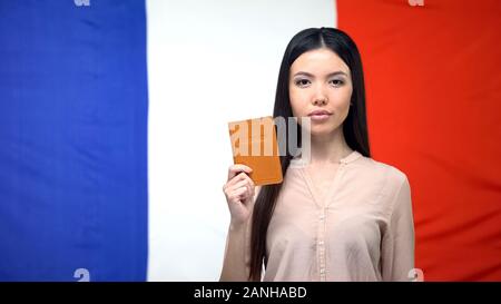 Grave femmina asiatica mostrando passaporto contro bandiera francese sfondo, Embassy Foto Stock