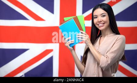 Bella femmina studente mostrando copybooks contro la bandiera britannica, apprendimento del linguaggio Foto Stock