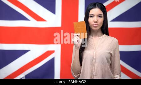 Fiducioso donna asiatica mostrando passaporto contro bandiera britannica, sfondo emigrante Foto Stock