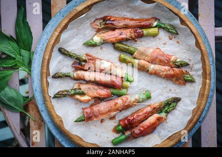 Cibo a buffet - prosciutto di Parma e mozzerella avvolto asparagi serviti su un piatto su una panchina da picnic rosa. Disposizione piatta Foto Stock