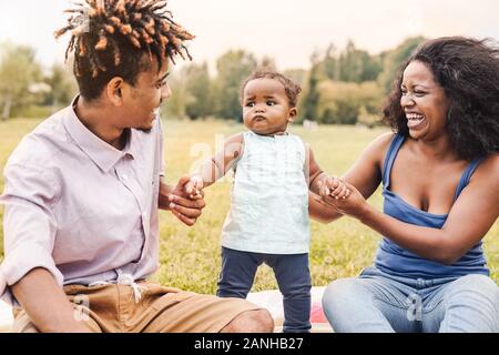 Felice famiglia africana per divertirsi insieme nel parco pubblico - Nero madre padre e figlia bambino godendo di bel tempo all'aperto Foto Stock