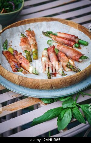 Cibo a buffet - prosciutto di Parma e mozzerella avvolto asparagi serviti su un piatto su una panchina da picnic rosa. Disposizione piatta Foto Stock