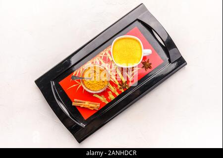 Tradizionale Indiano masala tea chai con spezie, cannella, anice e cardamomo in una tazza bianca su un originale Tray nero Foto Stock