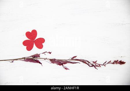 Secco ramo marrone rossiccio e cuori piegato a forma di quadrifoglio su una luce sullo sfondo di legno. Foto Stock