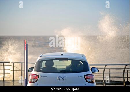 Giovane seduto in macchina guardando le onde su crash seawall a Cleveleys,UK Foto Stock