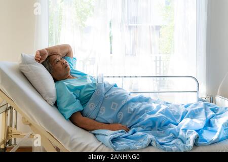 Asian premuto donna anziana paziente sdraiato sul letto guardando fuori dalla finestra in ospedale. Donna anziana pazienti è lieto recuperato dalla malattia. Foto Stock