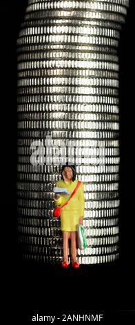 Figurina miniaturizzata femmina, che si trova davanti ad una pila di monete Foto Stock