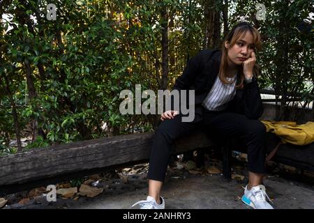 Capelli biondi donna con frangia di seduta sul tronco di legno e di pensiero circa la soluzione og il suo lavoro il problema. Foto Stock