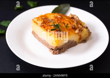 Concetto di cibo organico in casa di purè di patate casseruola di carne sul piatto di portata in ceramica bianca su ardesia nera sullo sfondo di pietra Foto Stock