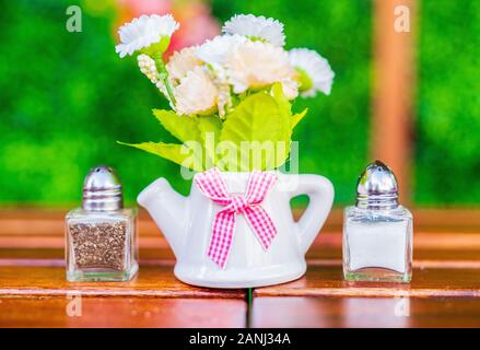 Teacup Floral Arrangiamento con sale e Pepe Shakers e sfondo verde. Foto Stock