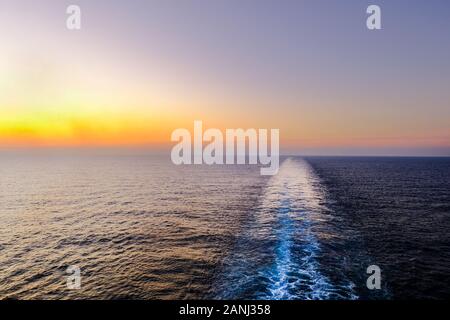 Un colpo delle navi sveglia preso dalla parte posteriore o poppa di una nave mentre si vendita attraverso il mare al tramonto. Foto Stock