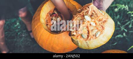 Banner con una stretta di mano d'uomo tira le sementi e materiale fibroso da una zucca prima della scultura per Halloween. jack-o-lantern. Foto Stock