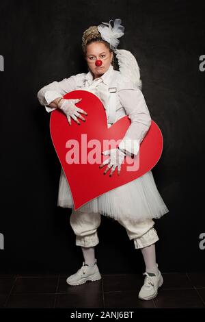 Clown donna posa con cuore rosso, ritratto in studio Foto Stock