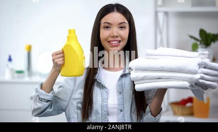 Donna sorridente che mostra gli asciugamani puliti e servizio lavanderia di detersivo e ammorbidente per tessuto Foto Stock