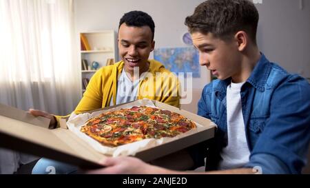 Due amici multirazziale apertura della casella con la pizza per la festa studentesca, Consegna del cibo Foto Stock