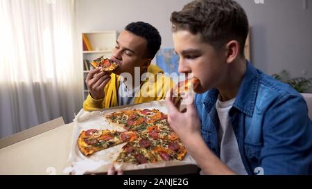 Afro-americani e caucasici amici adolescenti godendo la pizza, alimenti dannosi per la salute Foto Stock