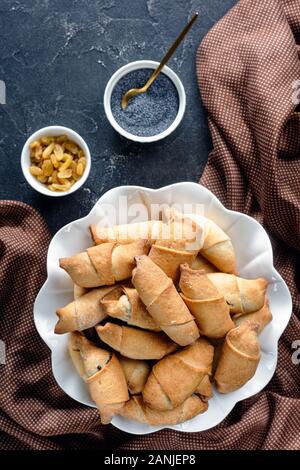 Pane appena sfornato mini croissant con semi di papavero e uvetta ripieno su una torta bianca stare su un tavolo in cemento, close-up, vista da sopra Foto Stock