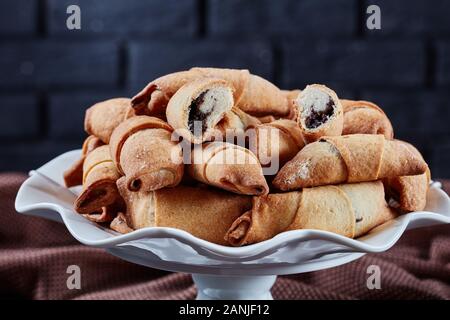 Pane appena sfornato mini croissant con semi di papavero e uvetta ripieno su una torta bianca riposare su una tavola di cemento con un muro di mattoni in background, clos Foto Stock