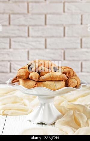 Pane appena sfornato mini croissant con semi di papavero e uvetta ripieno su una torta bianca riposare su una tavola di cemento con un muro di mattoni in background, clos Foto Stock