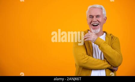 Stupito pensionato maschio esprimenti il gesto di wow contro lo sfondo arancione Foto Stock