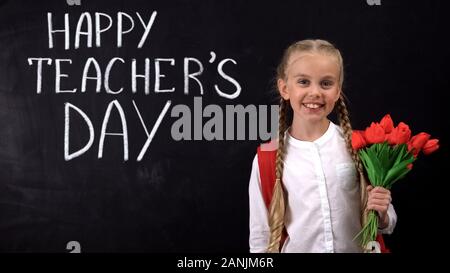 Gli insegnanti felice giorno scritti sulla lavagna, schoolgirl holding mazzo di tulipani Foto Stock