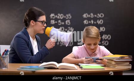 Naughty schoolboy ignorando insegnante con megafono giochi sul telefono Foto Stock