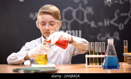 Ragazzo in occhiali protettivi la miscelazione di prodotti chimici liquidi in palloni, curioso genius Foto Stock