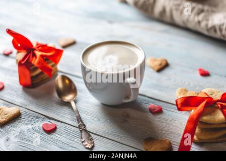 Tazza di caffè e un dolce dono del cookie legate con un nastro rosso a forma di cuore su un blu sullo sfondo di legno. Romantico San Valentino dono Foto Stock