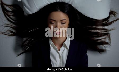 Imprenditrice in tuta di dormire sul letto, immaginando lei è a casa, concetto di fatica Foto Stock