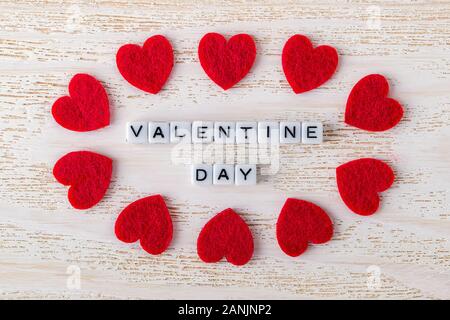 Iscrizione il giorno di San Valentino fatta di cubetti alfphabet circondato da feltro valentine cuori su di una superficie di legno. Biglietto di auguri con copia spazio. Il concetto di amore. Foto Stock