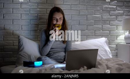 Premuto ragazza piange e mangiare a ciambella per superare lo stress, guardando film da soli Foto Stock