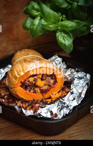 Zucca di Butternut ripiena arrosto con insalata di cavolo e ceci. Sano cibo vegano servito su un vassoio arancione con sfondo nero. Vista dall'alto / Foto Stock