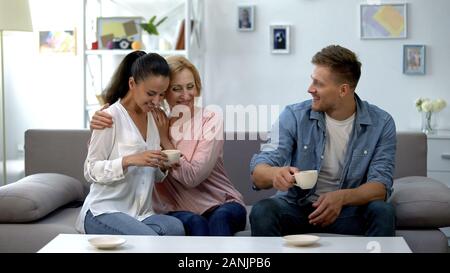 Sorridente madre abbracciando la figlia durante la riunione di famiglia, bere il tè a casa Foto Stock