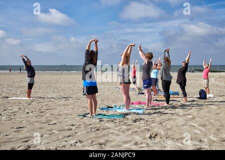 Praticante di yoga femminile che offre una lezione di yoga a un gruppo di donne sulla spiaggia meridionale dell'isola di Borkum Foto Stock