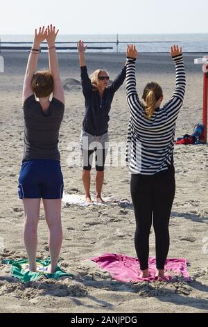 Praticante di yoga femminile che offre una lezione di yoga a un piccolo gruppo di donne sulla spiaggia meridionale dell'isola di Borkum Foto Stock