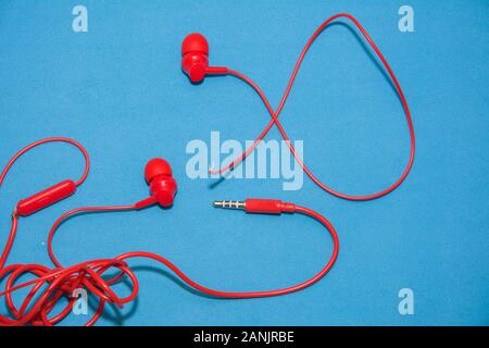 Rosso strappato rotto le cuffie sul classico sfondo blu. Close up rotto vecchio auricolare Foto Stock