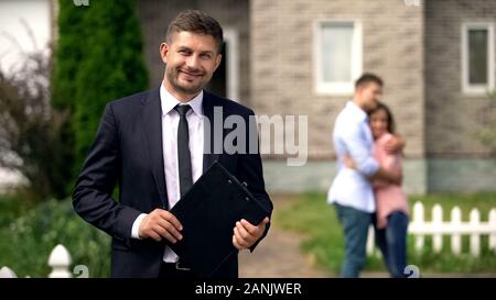 Broker sorridente in piedi con documenti, Famiglia Felice costeggiata vicino la loro nuova casa Foto Stock