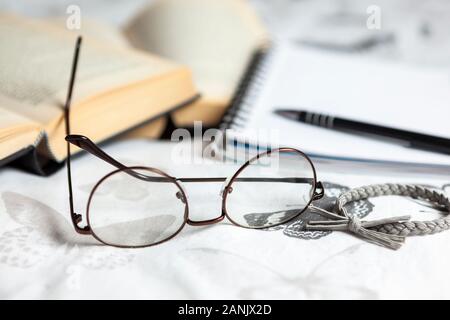 Coppia di occhiali da lettura e una fascia per capelli su un letto con alcuni libri e un blocco note Foto Stock