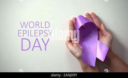 Mondo epilessia giorno iscrizione, nastro viola a lady mani, la consapevolezza della malattia Foto Stock
