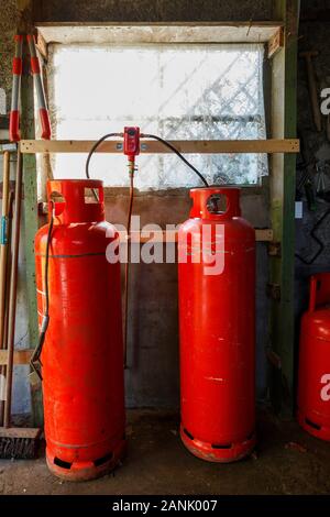 Due grandi rosso bottiglie di gas davanti a una finestra in un vecchio capannone. Foto Stock