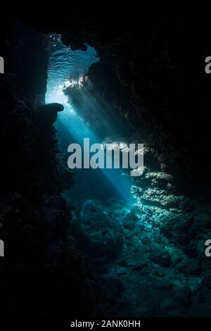 Fasci di luce del sole entrano in una caverna subacquea scura erosa in una barriera corallina nelle Isole Salomone. Le barriere coralline sono spesso fregate di grotte e fessure. Foto Stock