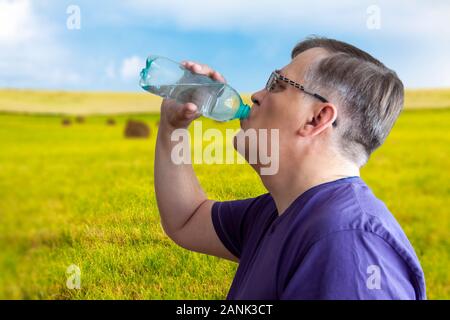 Un uomo beve acqua da una bottiglia. Foto Stock