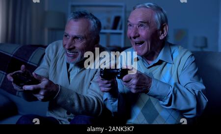 Emotivo maschi anziani amici holding joystick per la riproduzione di video gioco, divertimento Foto Stock