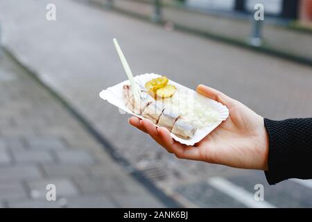Holland aringa pesce in mano femminile al di fuori. Olandese tradizionale cibo di strada, aringa pesce. Stock photo street food, aringa pesce con cipolle e sottaceti Foto Stock